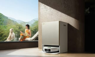 A modern white air treatment appliance standing in a bright living room with a large window overlooking green hills