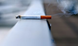 Lit cigarette resting on a ledge with smoke wisps rising - Photo by Andres Siimon on Unsplash