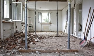 Home renovation in progress with paint cans, sanding equipment, and visible dust particles in the air