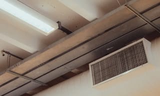 Person checking an indoor air quality monitor displaying CO2 and PM2.5 readings