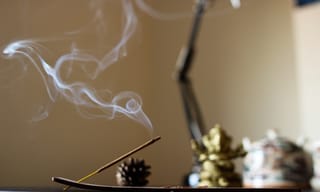 Incense stick burning with a thin stream of smoke rising in a dimly lit room