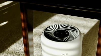 White Levoit air purifier running under a table in a sunlit room, illustrating everyday energy use