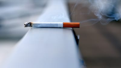 Lit cigarette resting on a ledge with smoke wisps rising - Photo by Andres Siimon on Unsplash