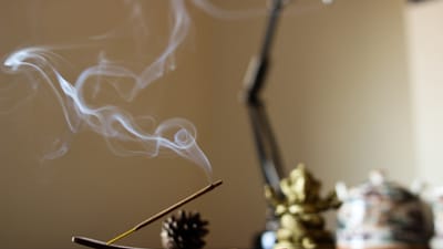 Incense stick burning with a thin stream of smoke rising in a dimly lit room