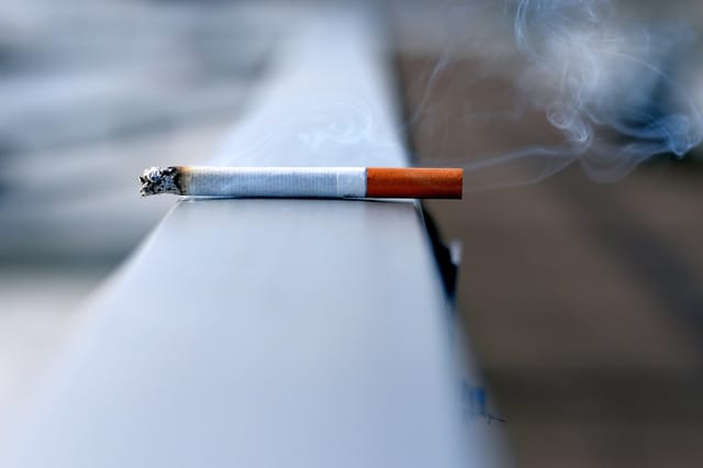 Lit cigarette resting on a ledge with smoke wisps rising - Photo by Andres Siimon on Unsplash