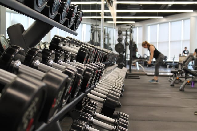 Dumbbell rack in a gym with exercise equipment and natural light. Photo from Unsplash