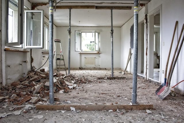 Home renovation in progress with paint cans, sanding equipment, and visible dust particles in the air