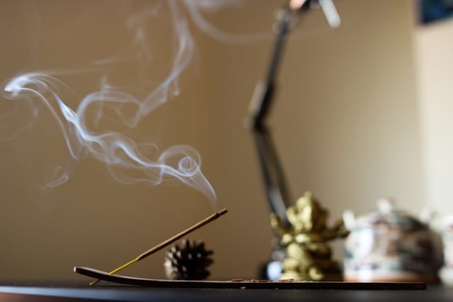 Incense stick burning with a thin stream of smoke rising in a dimly lit room